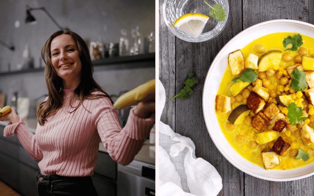 Leende, brunhårig kvinna i rosa tröja står i ett kök med bananer i händerna. En tallrik fylld med gul kikärtscurry.
