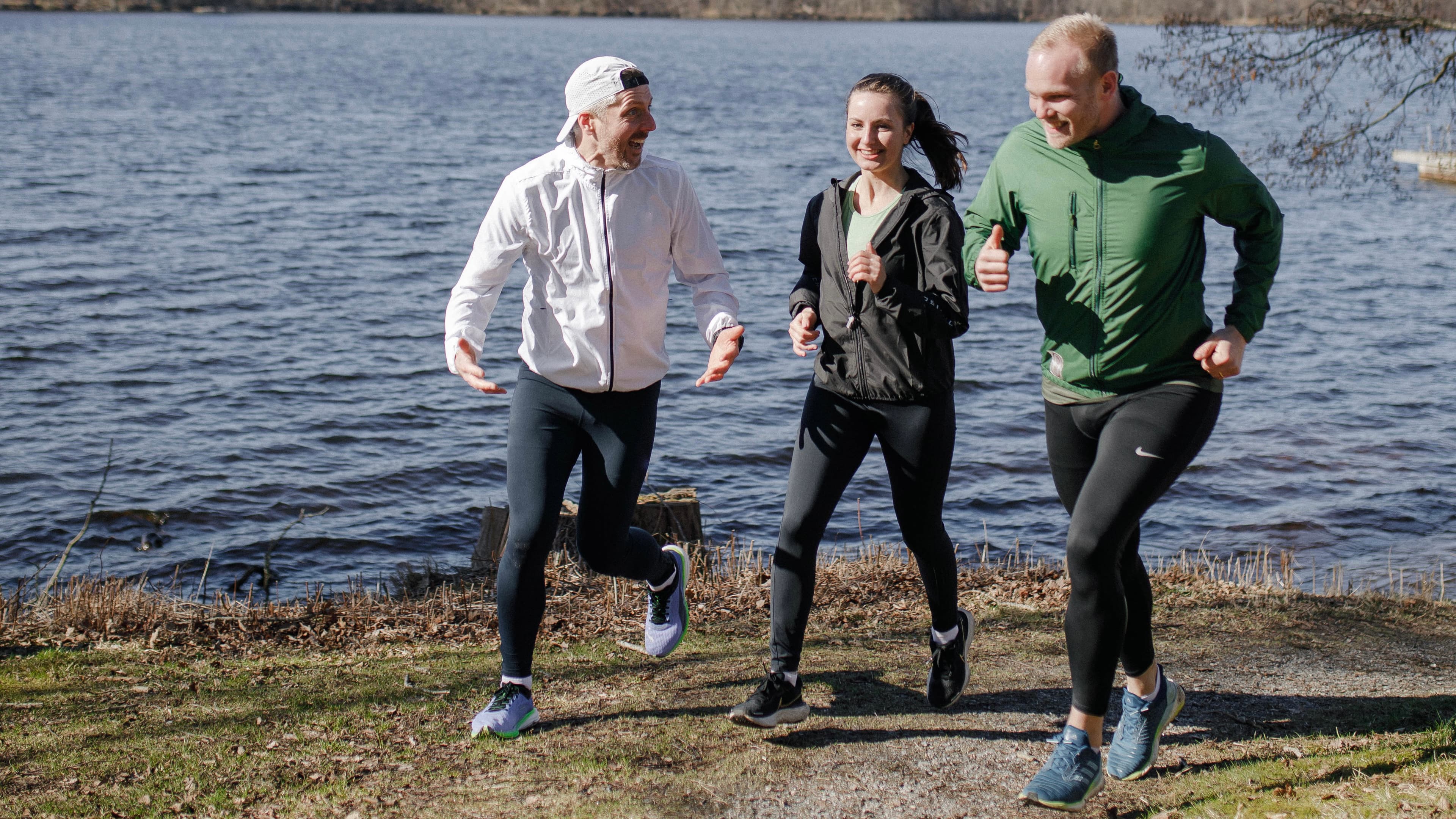 Tre personer löptränar vid vattnet och pratar samtidigt med varandra.