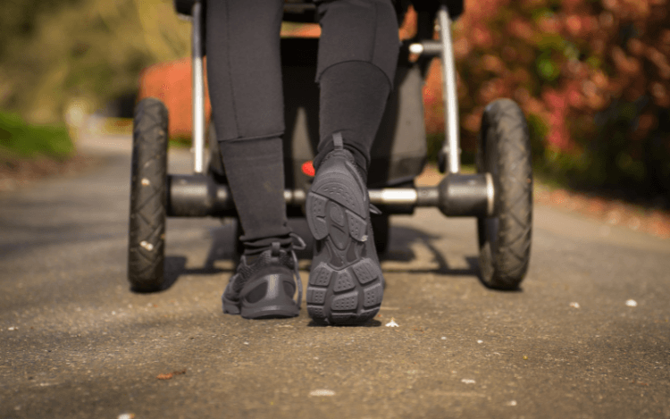 Närbild på en persons skor som promenerar med en vagn under hösten.