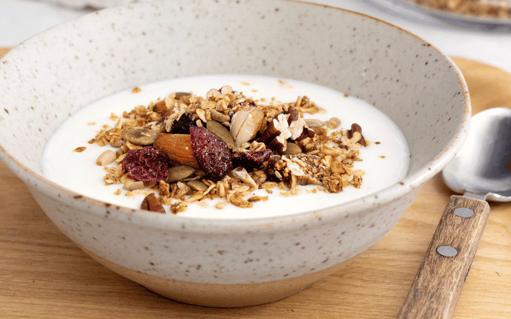 Skärbräda med skål fylld med hemmagjord granola och yoghurt.