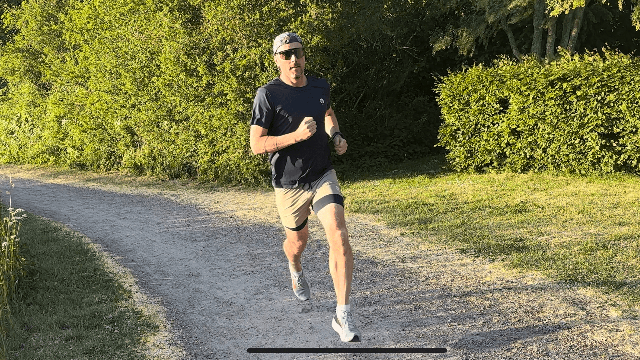 En man med solglasögon och balåtvänd keps springer på en väg