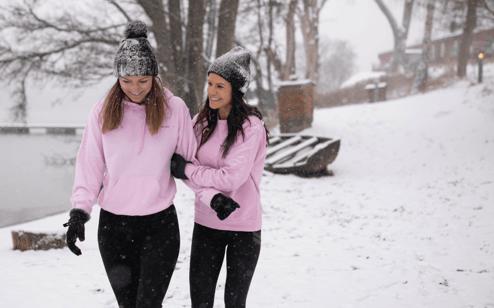 Två kvinnor med rosa tröjor står och pratar i snön.