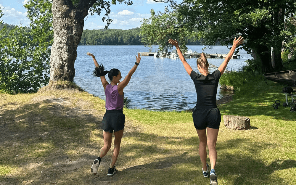 Två kvinnor som demonstrerar känslan av att springa en mil genom att springa på en gräsmatta och sträcka upp händerna i luften.