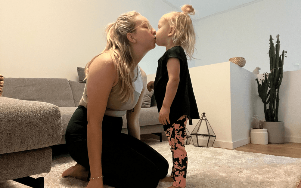 Mamma pussar sin dotter på munnen.