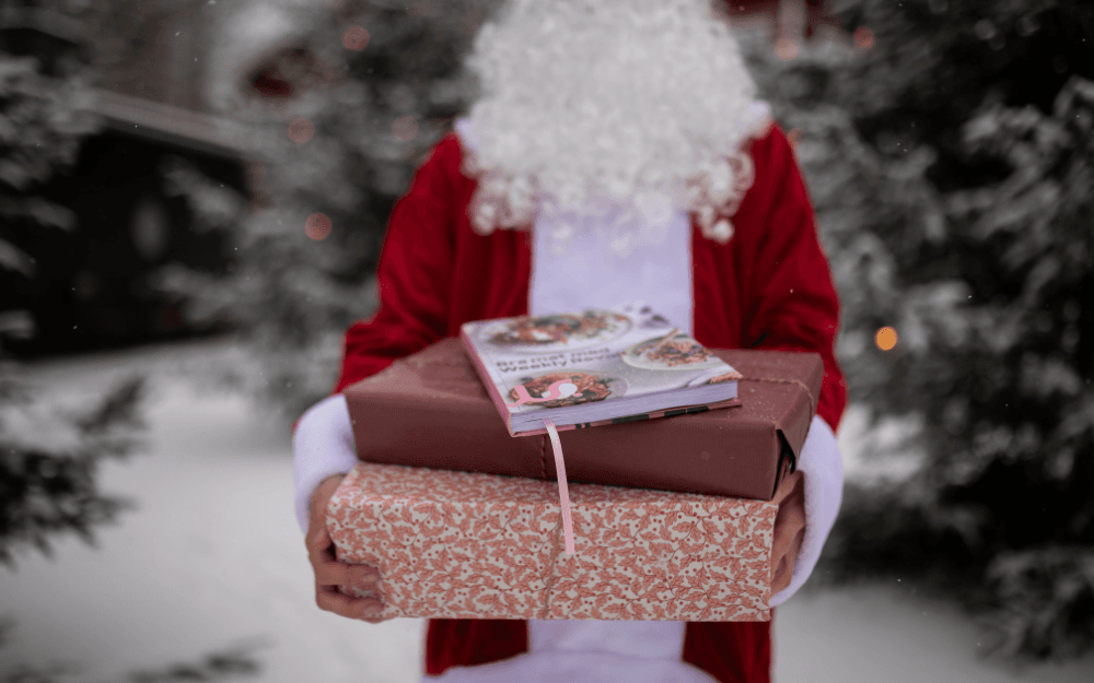 Tomte håller i två julklappar. Ovanpå ligger boken "Bra mat med Weekly Revolt"
