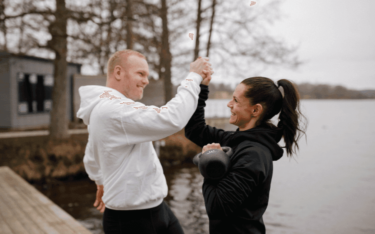 Kvinna och man tränar på brygga, kvinna håller i kettle bell och de peppar varandra.