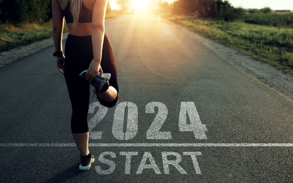 Bild som visar på hur vi startar nyår med nya mål. Det står Start 2024 på marken och en kvinna som ska springa stretchar.