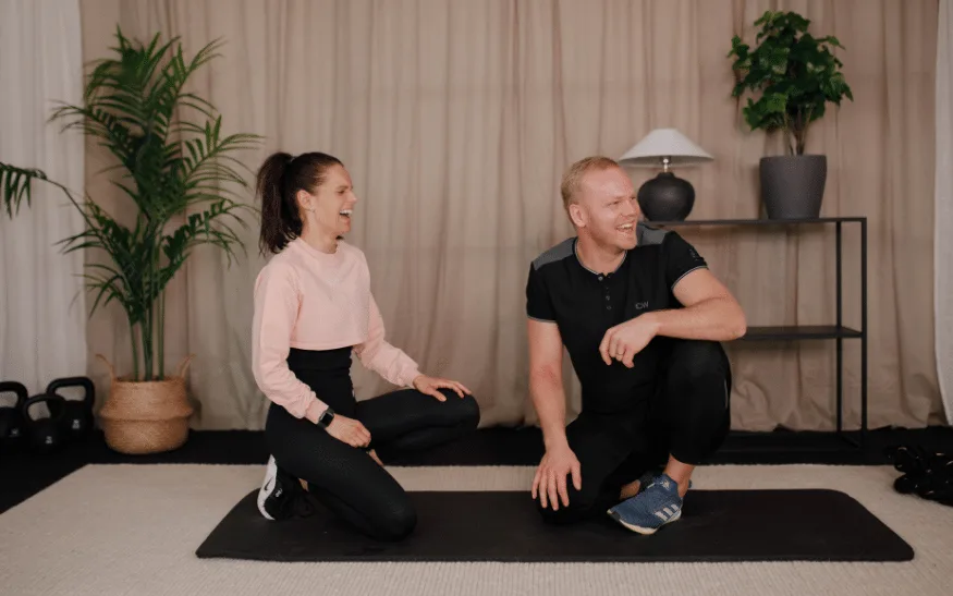 Kvinna och man sitter på en träningsmatta och skrattar.