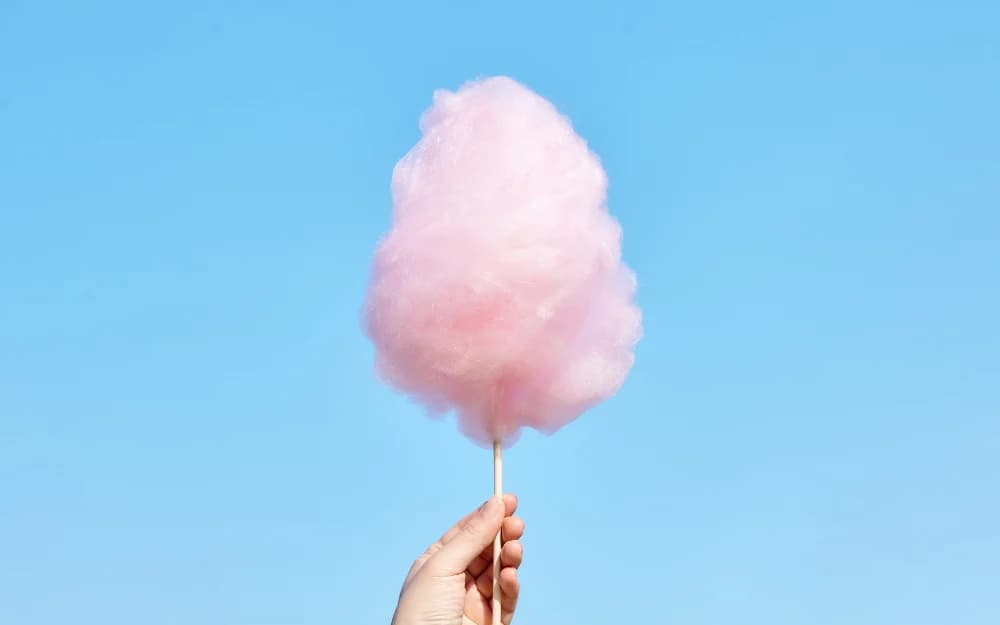 En hand håller rosa sockervadd framför en blå bakgrund.