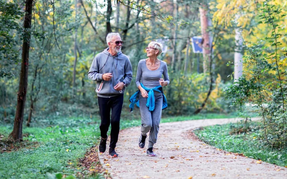 Ett äldre par i grå kläder är ute och joggar tillsammans på en skogsslinga