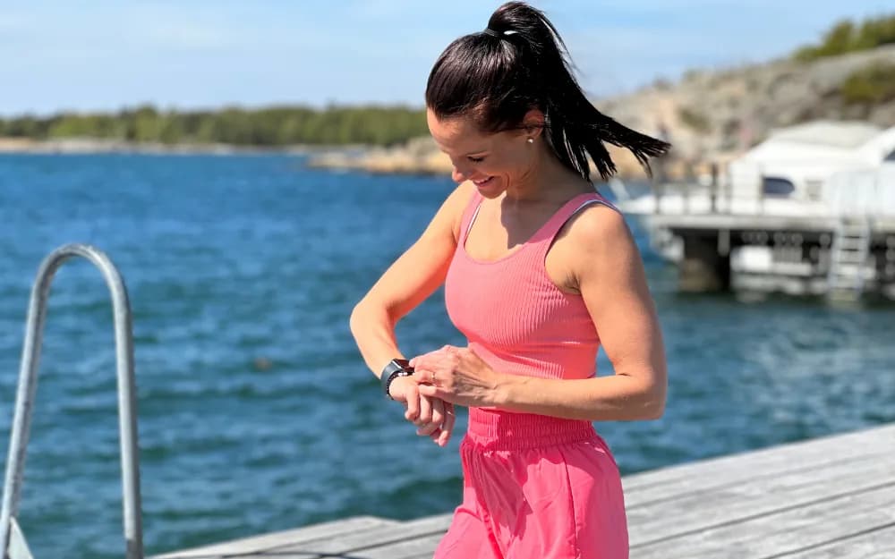 Kvinna med rosa träningskläder står på en brygga och tittar på sin träningsklocka