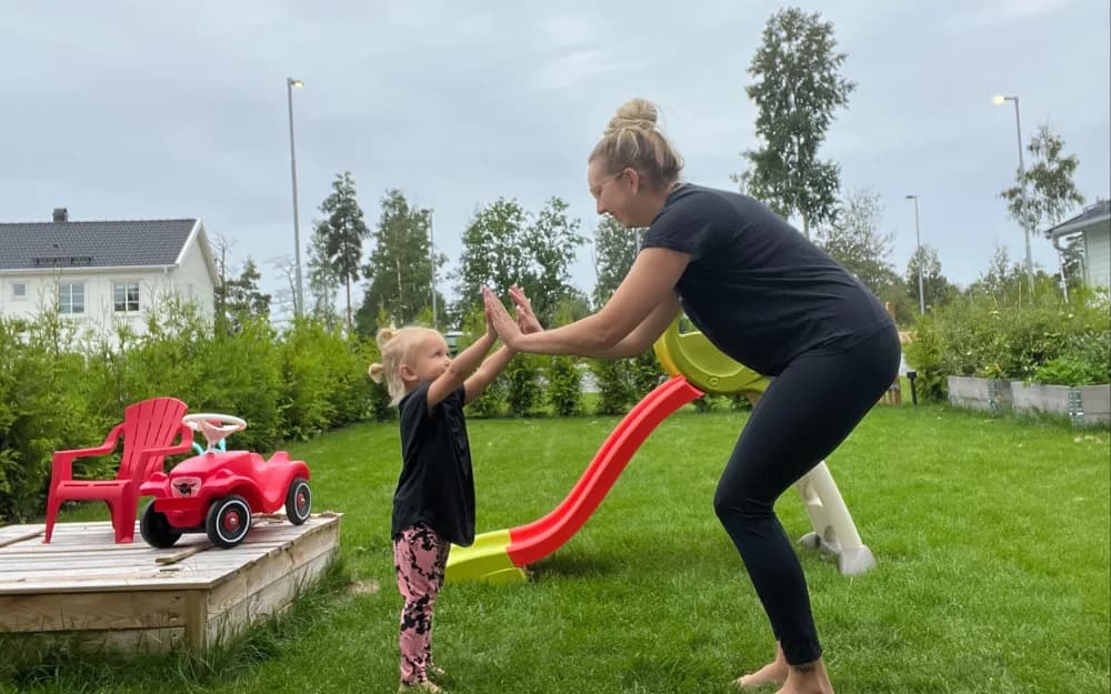 Kvinna tränar i sin trädgård och gör high five med sin dotter.