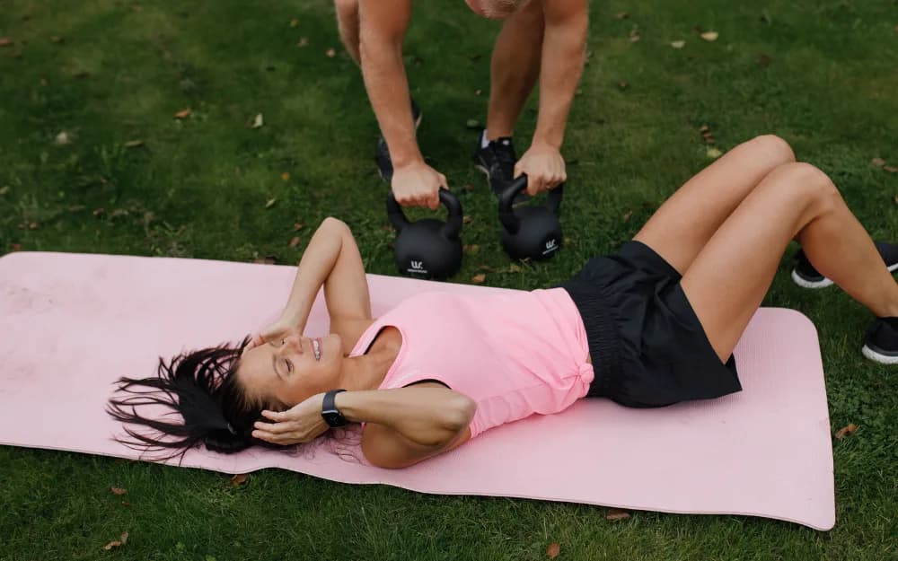 Kvinna med rosa topp och svarta shorts gör situps på en rosa träningsmatta.
