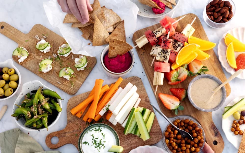 Brickor med plockmat – grönsaksstavar, fruktspett, jordgubbar och skålar med oliver, ärtor, kikärtor med mera.