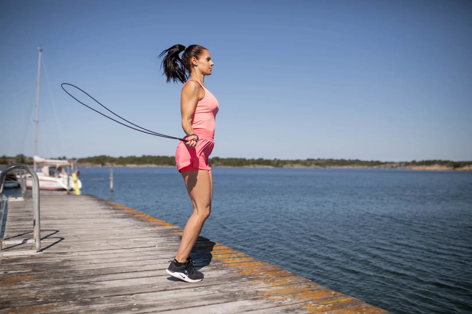 Kvinna med rosa shorts och rosa linne hoppar hopprep på en brygga