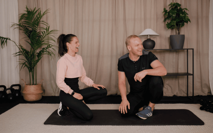 Kvinna och man sitter på en träningsmatta och skrattar.