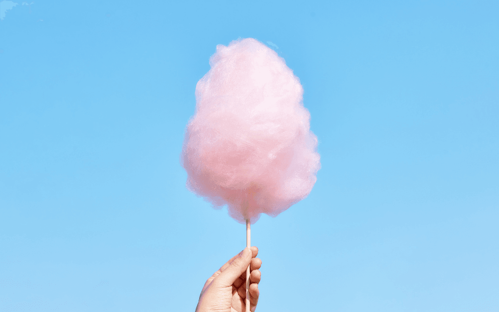 En hand håller rosa sockervadd framför en blå bakgrund.