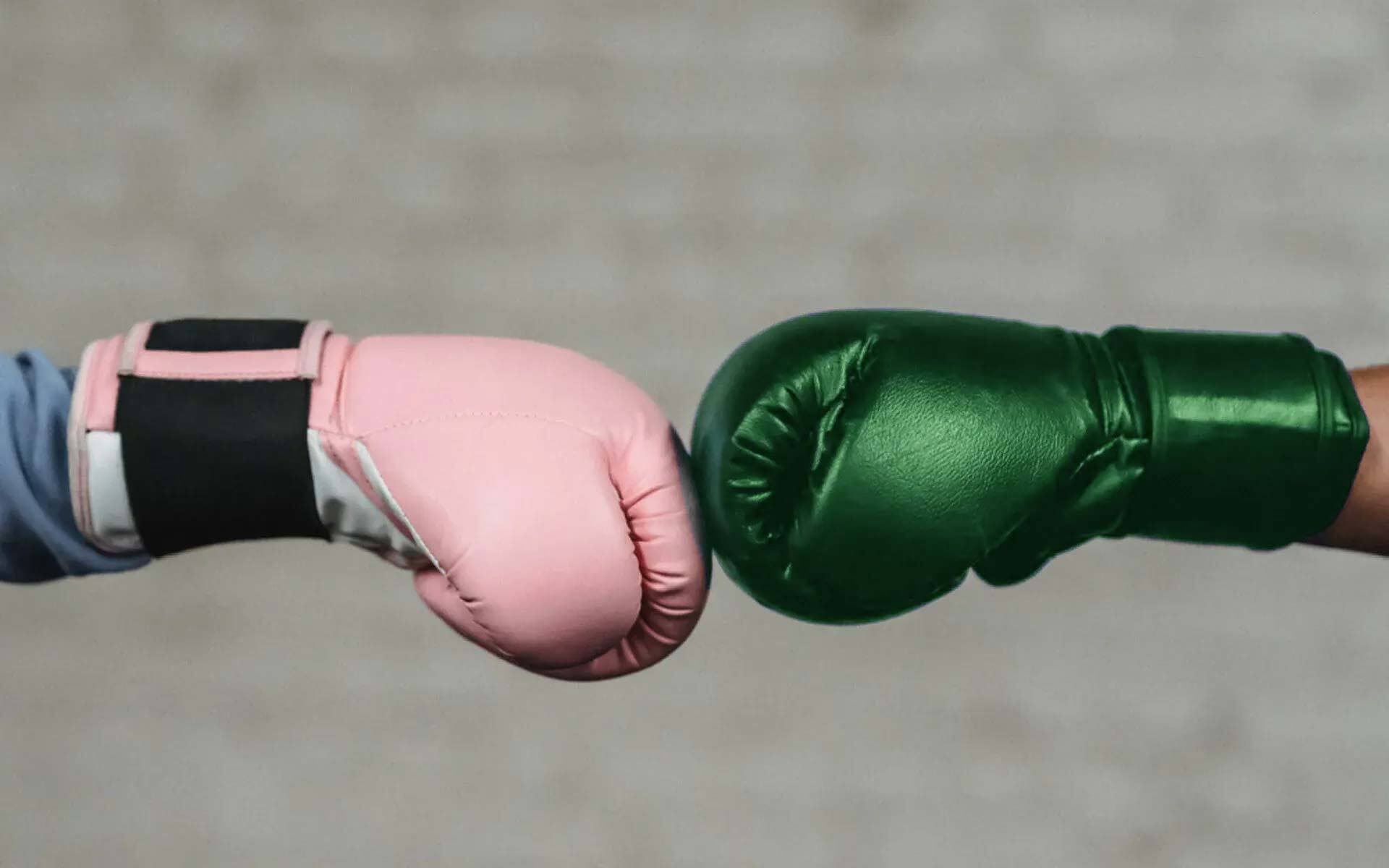 En rosa boxningshandske slår mot en grön boxningshandske
